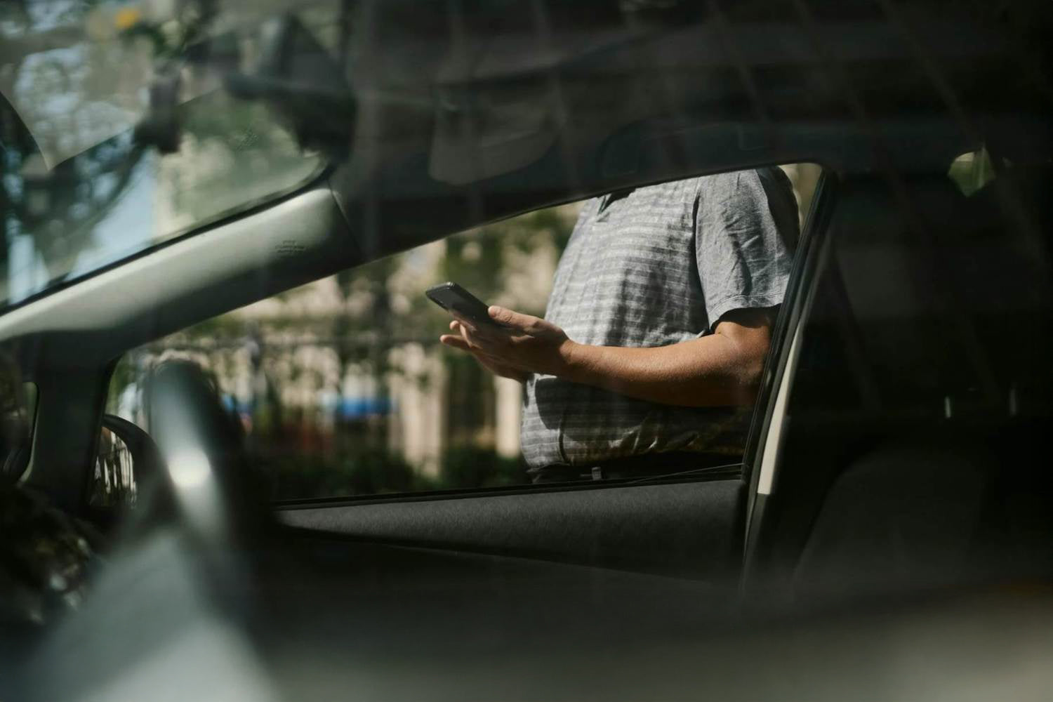 Zdjęcie z perspektywy kierowcy na osobę znajdującą się na zewnątrz auta z smartfonem w ręku.