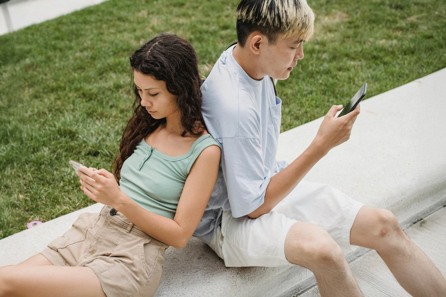 Dwie osoby opare plecami do siebie i przeglądające dwa smartfony.